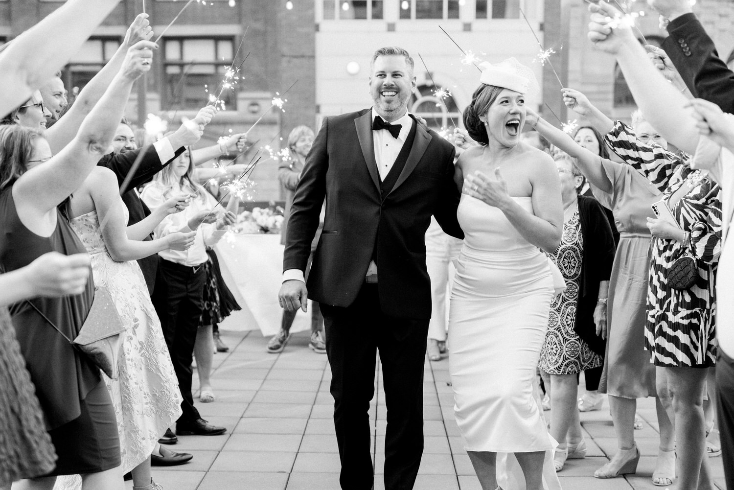 A joyful couple walks through a crowd of guests holding sparklers at their wedding reception, capturing a moment of celebration and love.