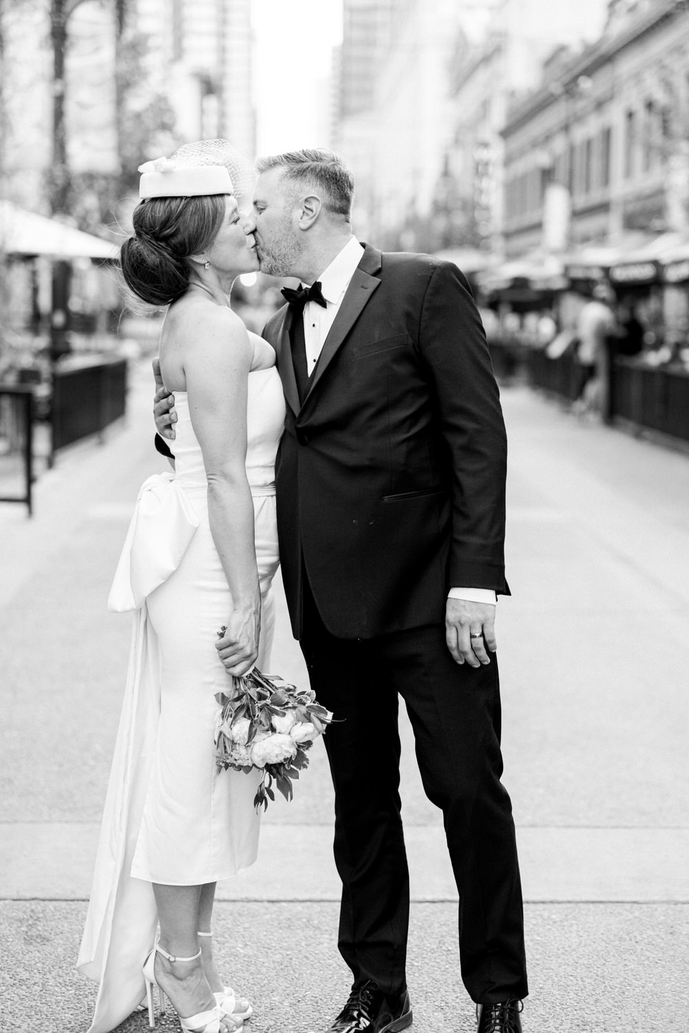 Romantic black-and-white image of a bride and groom sharing a kiss on a city street, showcasing love and elegance.