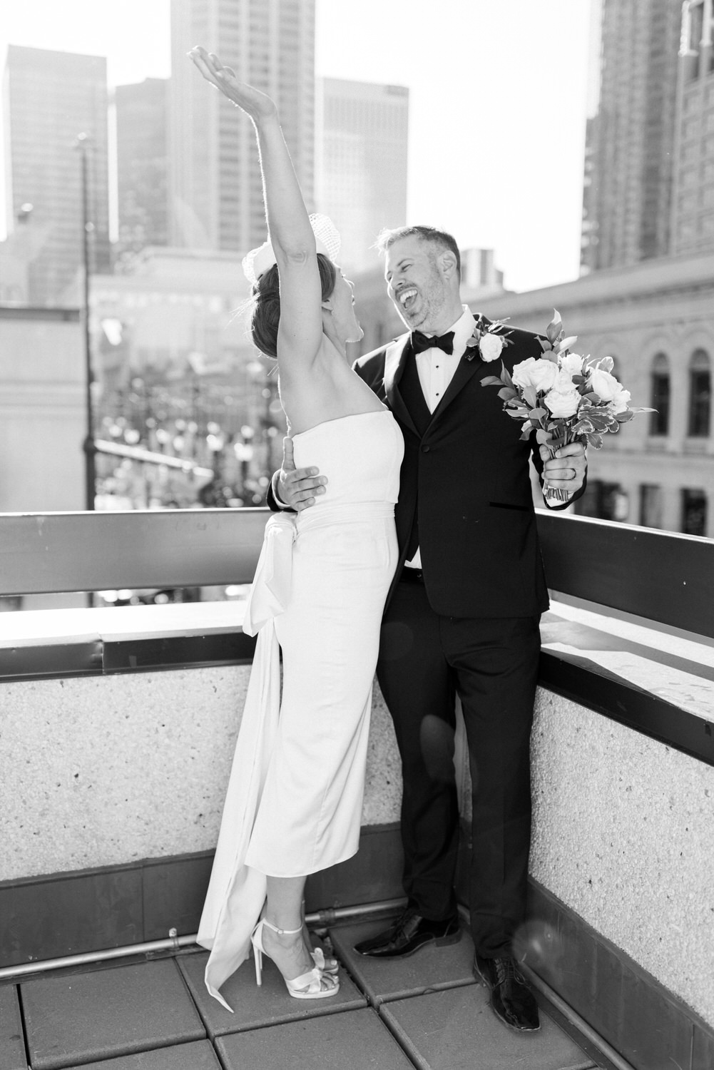 Joyful Wedding Celebration::A couple embraces on a balcony, celebrating their wedding with laughter and love against a city backdrop.