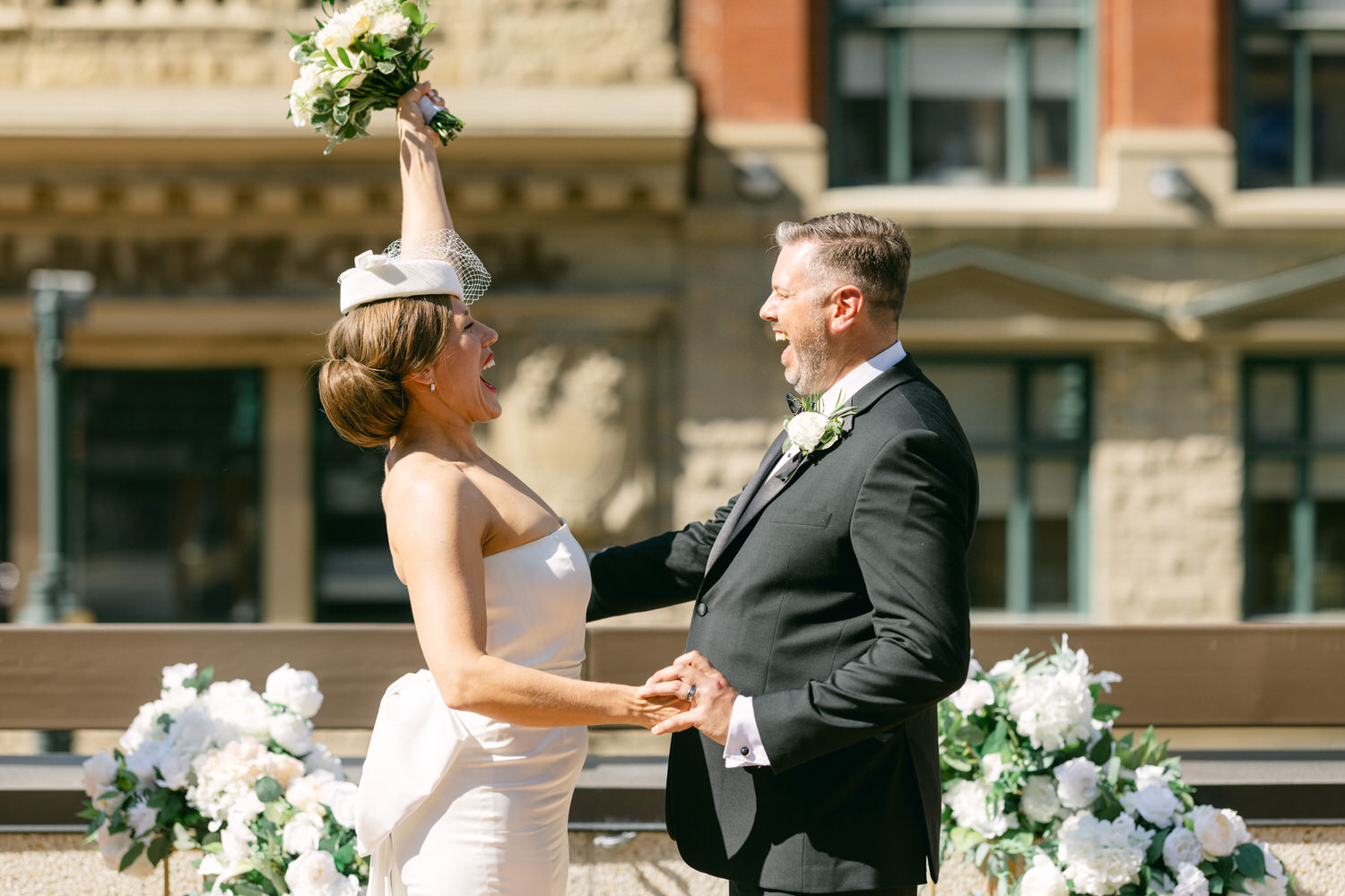 A bride and groom share a moment of joy during their outdoor wedding ceremony, surrounded by elegant floral arrangements.