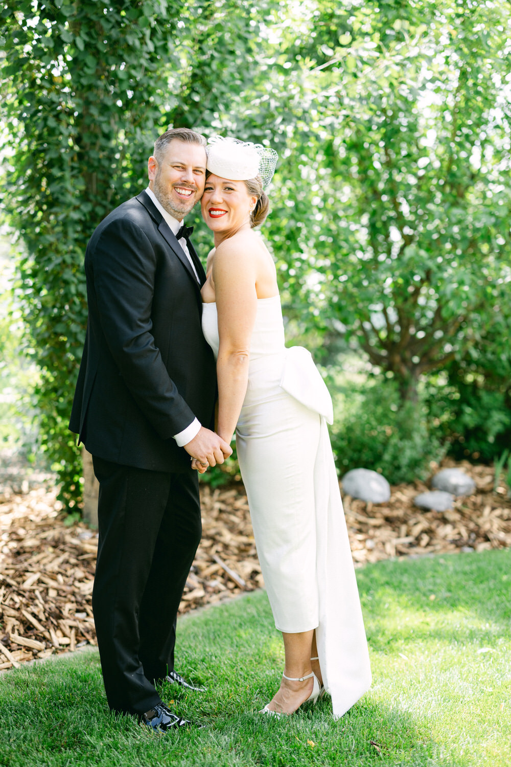 A happy couple smiles and holds hands in a lush green garden, showcasing vibrant greenery and natural beauty.