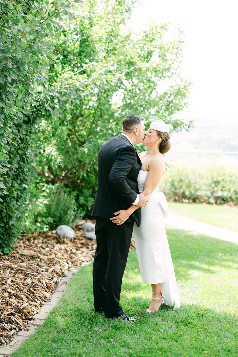 A couple shares a kiss in a lush garden setting, showcasing love and intimacy amidst greenery.