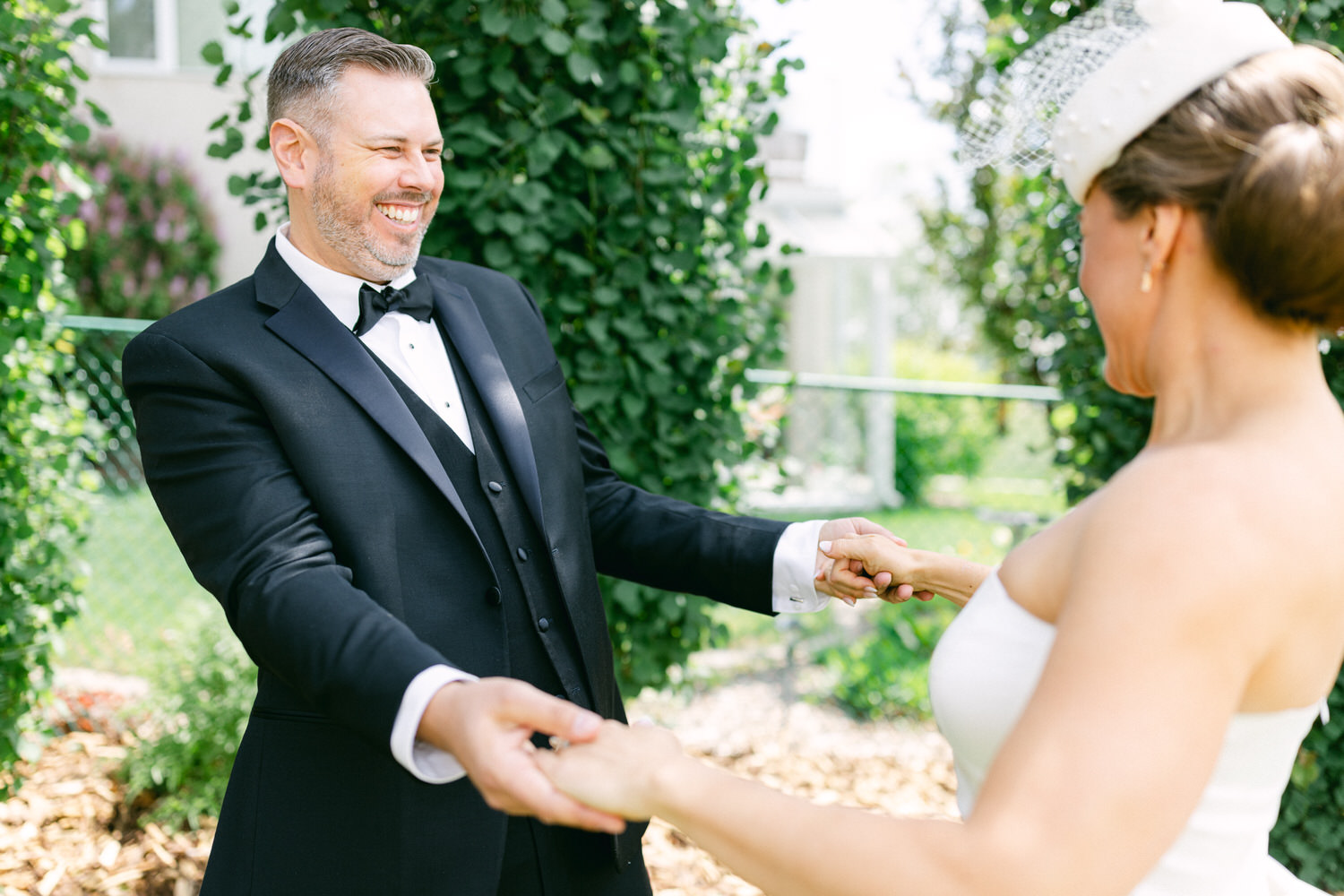 A joyful couple sharing a romantic moment outdoors, with the groom in a tuxedo and the bride in a strapless dress, surrounded by greenery.