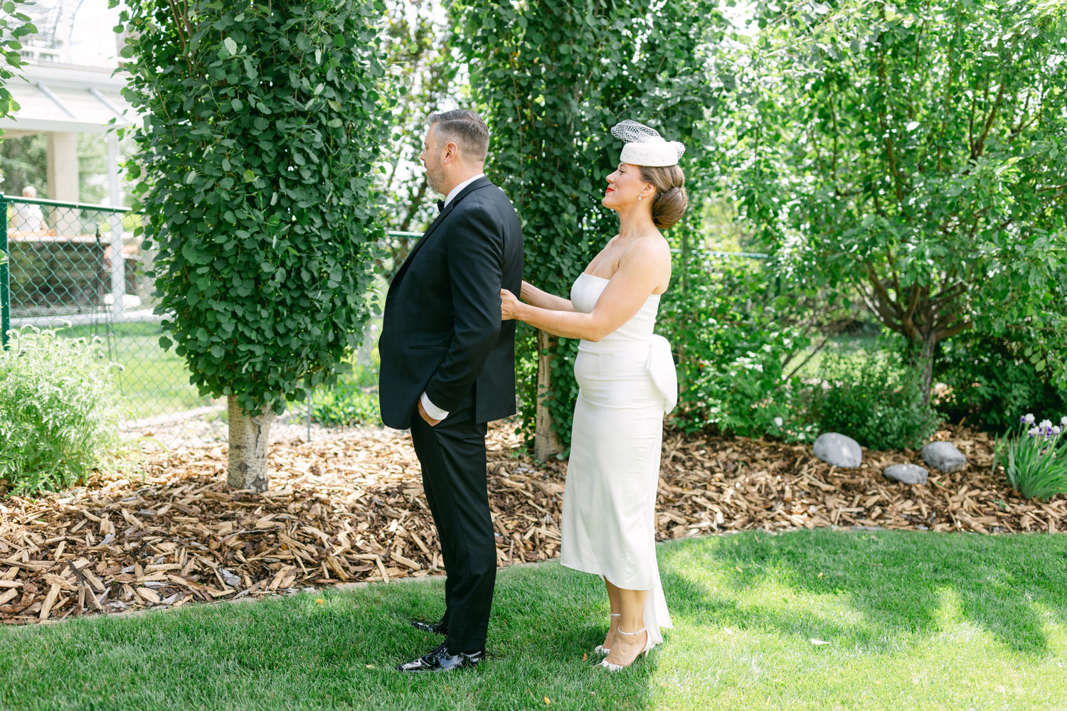 A bride adjusts her groom's suit while standing together in a lush garden, capturing a heartfelt pre-wedding moment.