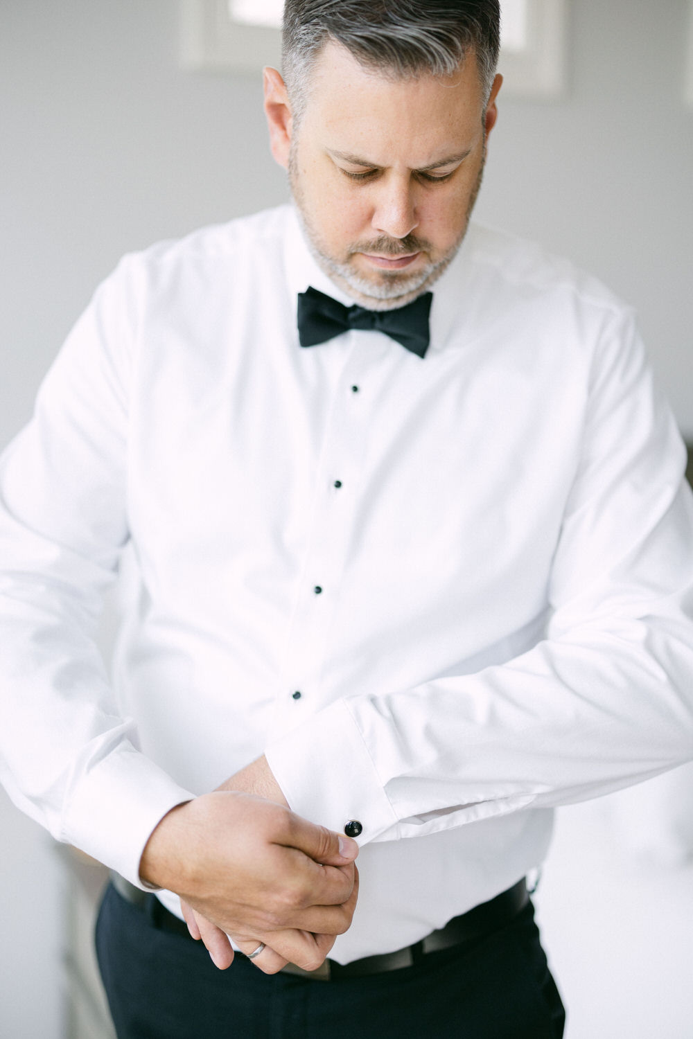 Man adjusting his cufflinks while wearing a white dress shirt and black bow tie, focusing on details before the wedding.