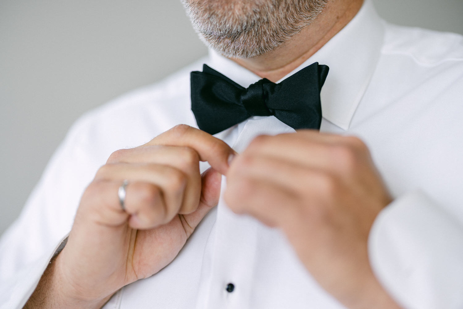 Close-up of a man adjusting his black bow tie while wearing a white dress shirt.