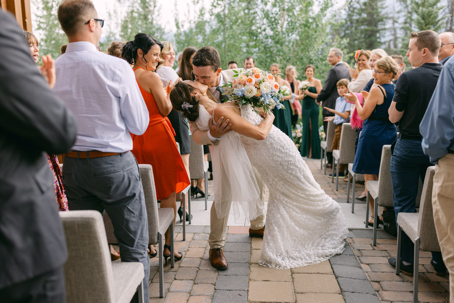 A joyful couple sharing a kiss during their wedding, surrounded by enthusiastic guests applauding and cheering.