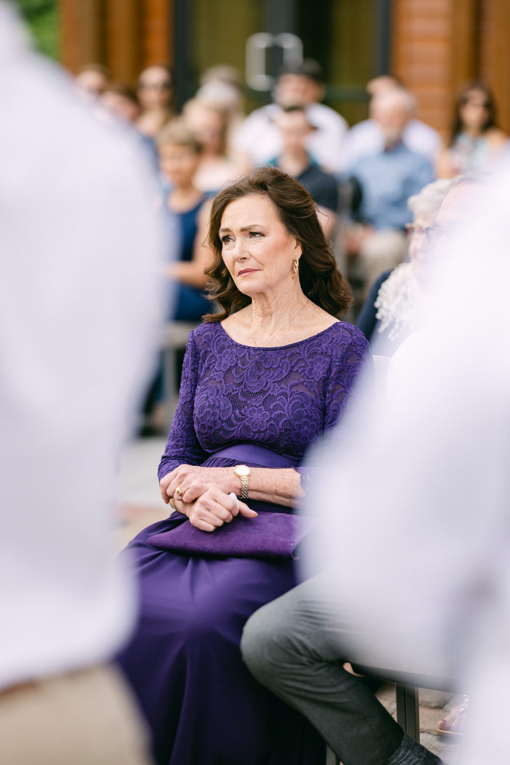 A woman in a purple dress seated among guests at an outdoor ceremony, appearing contemplative and engaged.