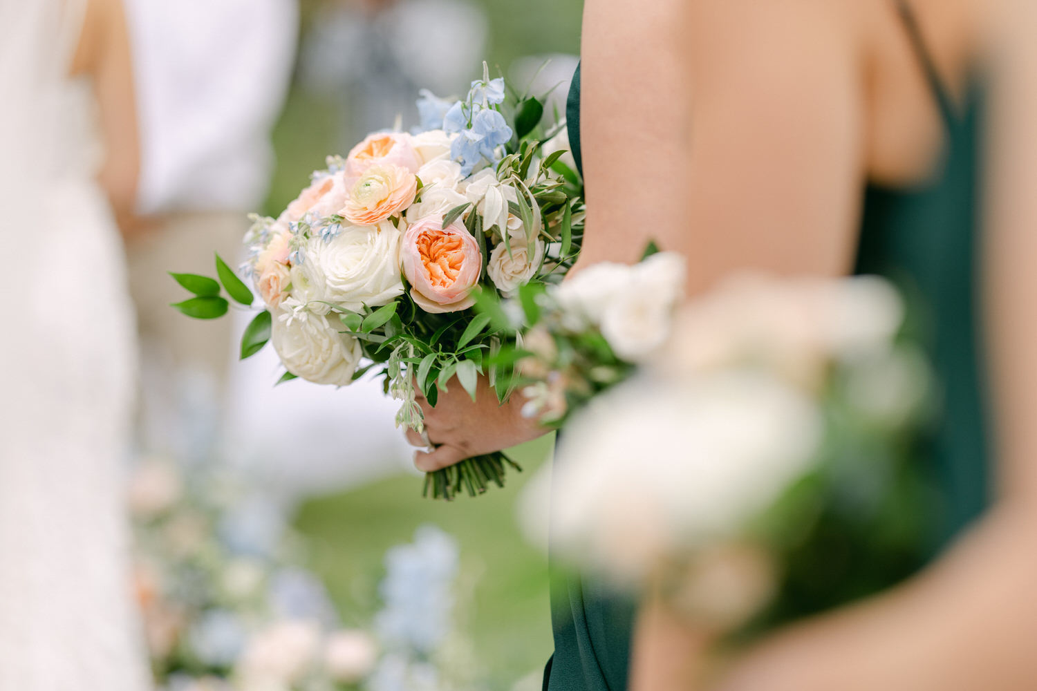 Close-up of a beautiful floral bouquet featuring peonies, roses, and greenery held by a bridesmaid during a wedding ceremony.