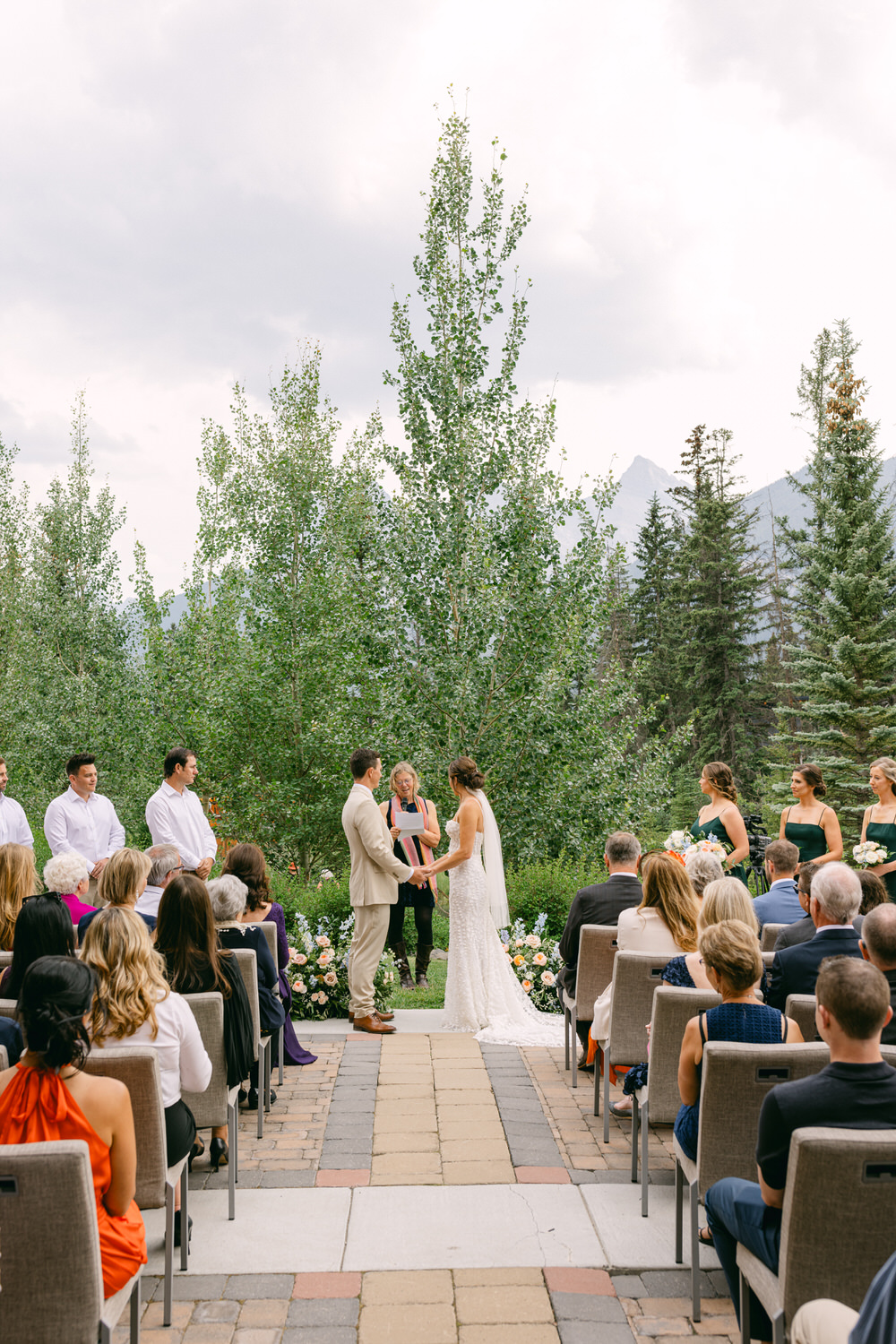 A couple exchanges vows during their outdoor wedding ceremony surrounded by guests and lush greenery in a scenic setting.