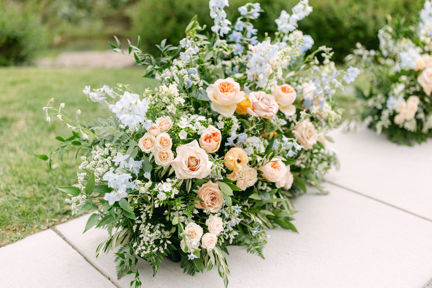 A beautiful display of peach roses and delicate blue flowers arranged artistically on a lush green lawn.