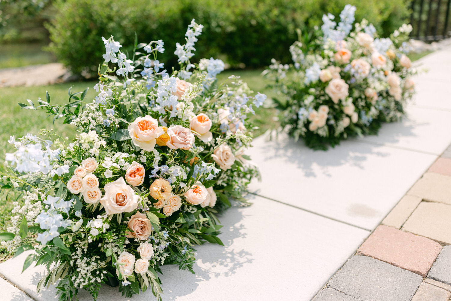 Beautiful floral arrangements featuring soft peach and blue flowers, placed beside a pathway on a sunny day.