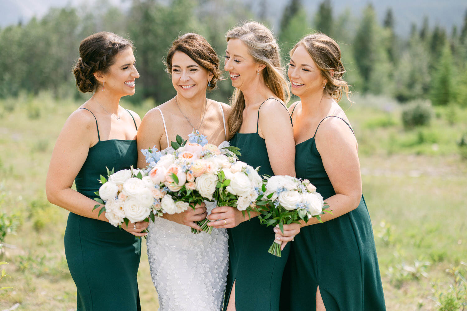 A cheerful bride surrounded by her bridesmaids in elegant green dresses, holding beautiful floral bouquets in a picturesque outdoor setting.