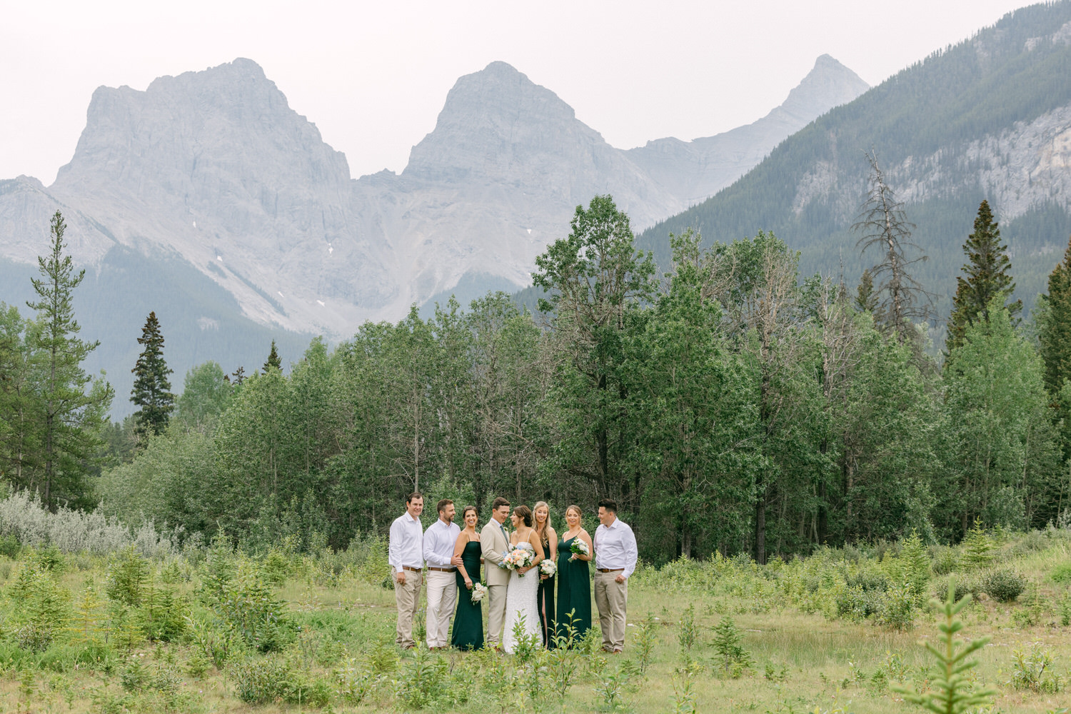 Bridal party posing in a lush green field with mountains in the background.