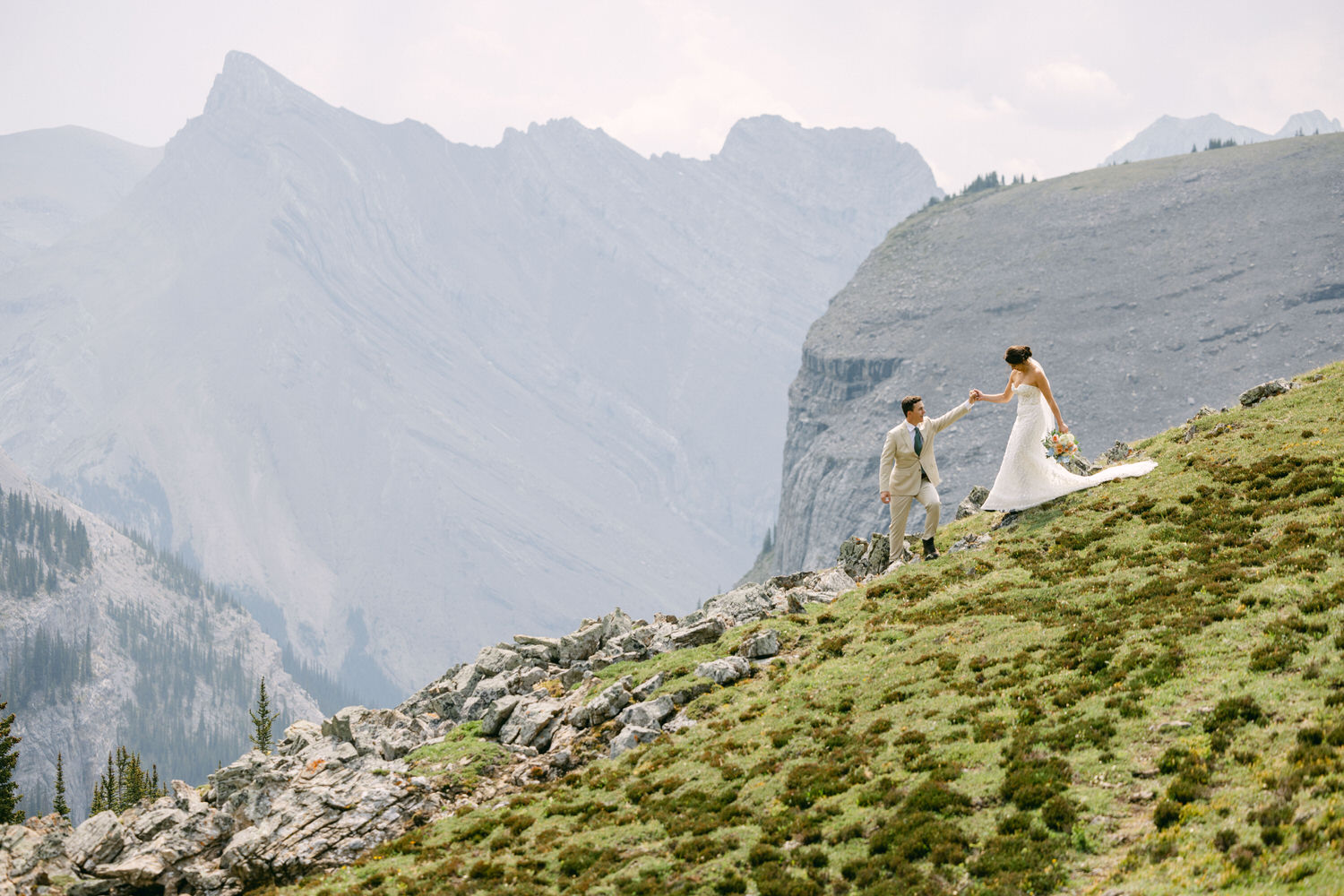 A happy couple enjoying their wedding day on a rocky mountain slope with breathtaking views in the background.