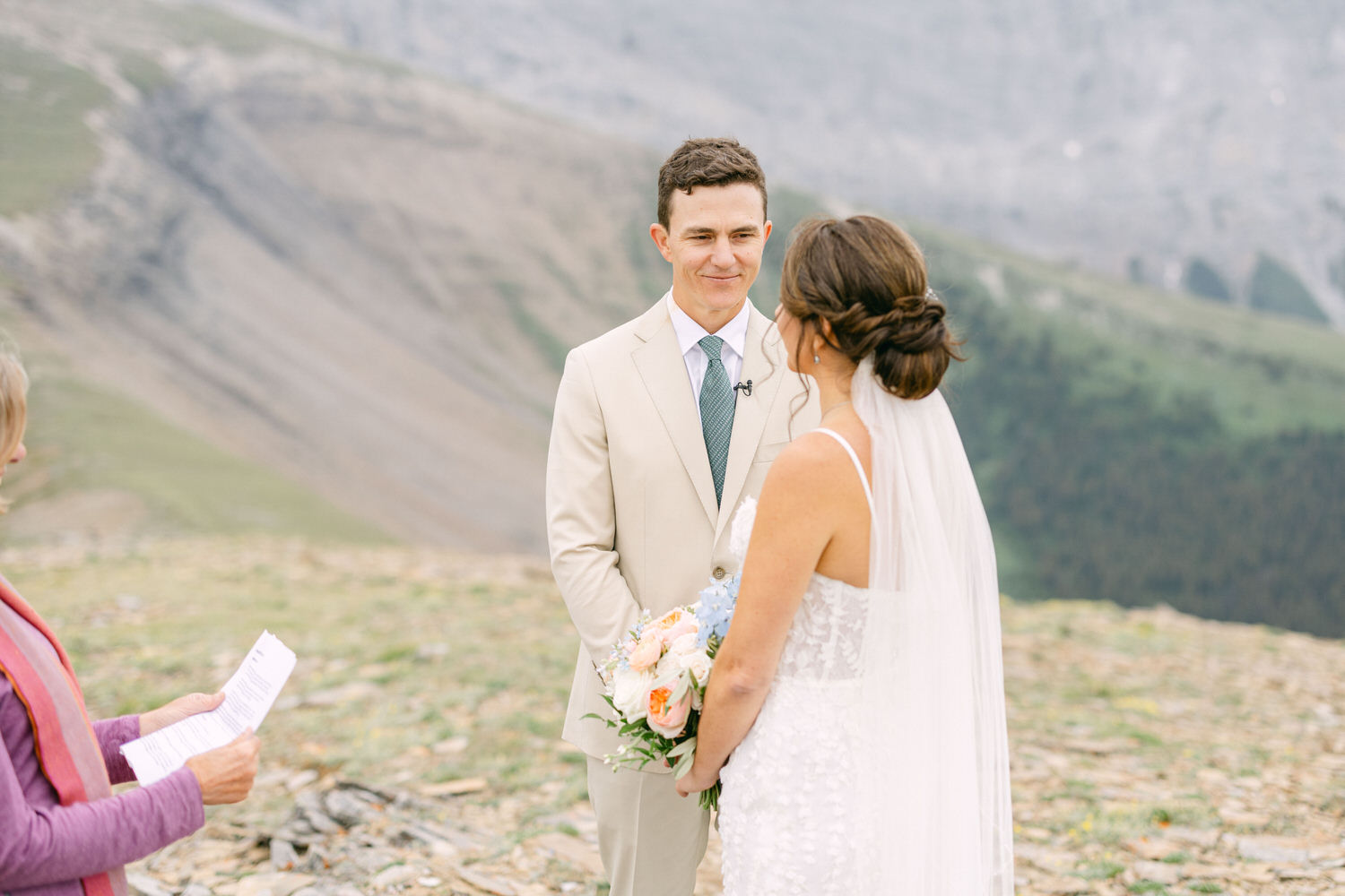 A couple exchanges vows during an intimate outdoor wedding ceremony in a mountainous landscape, surrounded by nature.