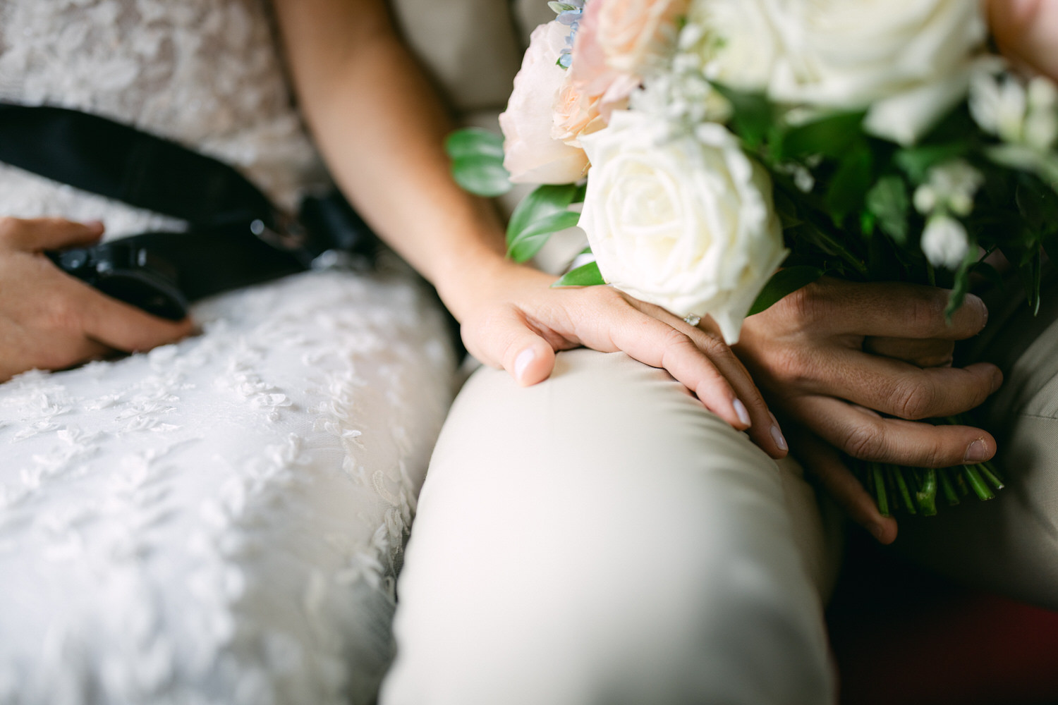 Close-up of a bride's hand holding a bouquet, resting on a groom's hand in an intimate setting.