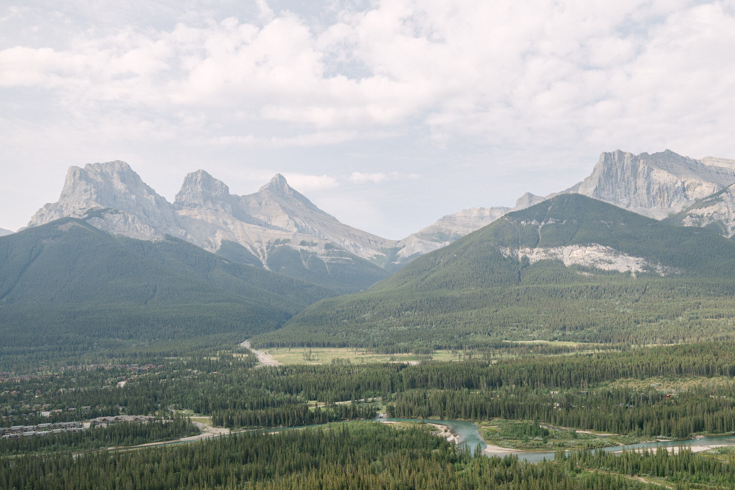 A scenic view of rugged mountains bordered by dense forests and winding rivers under a cloudy sky.