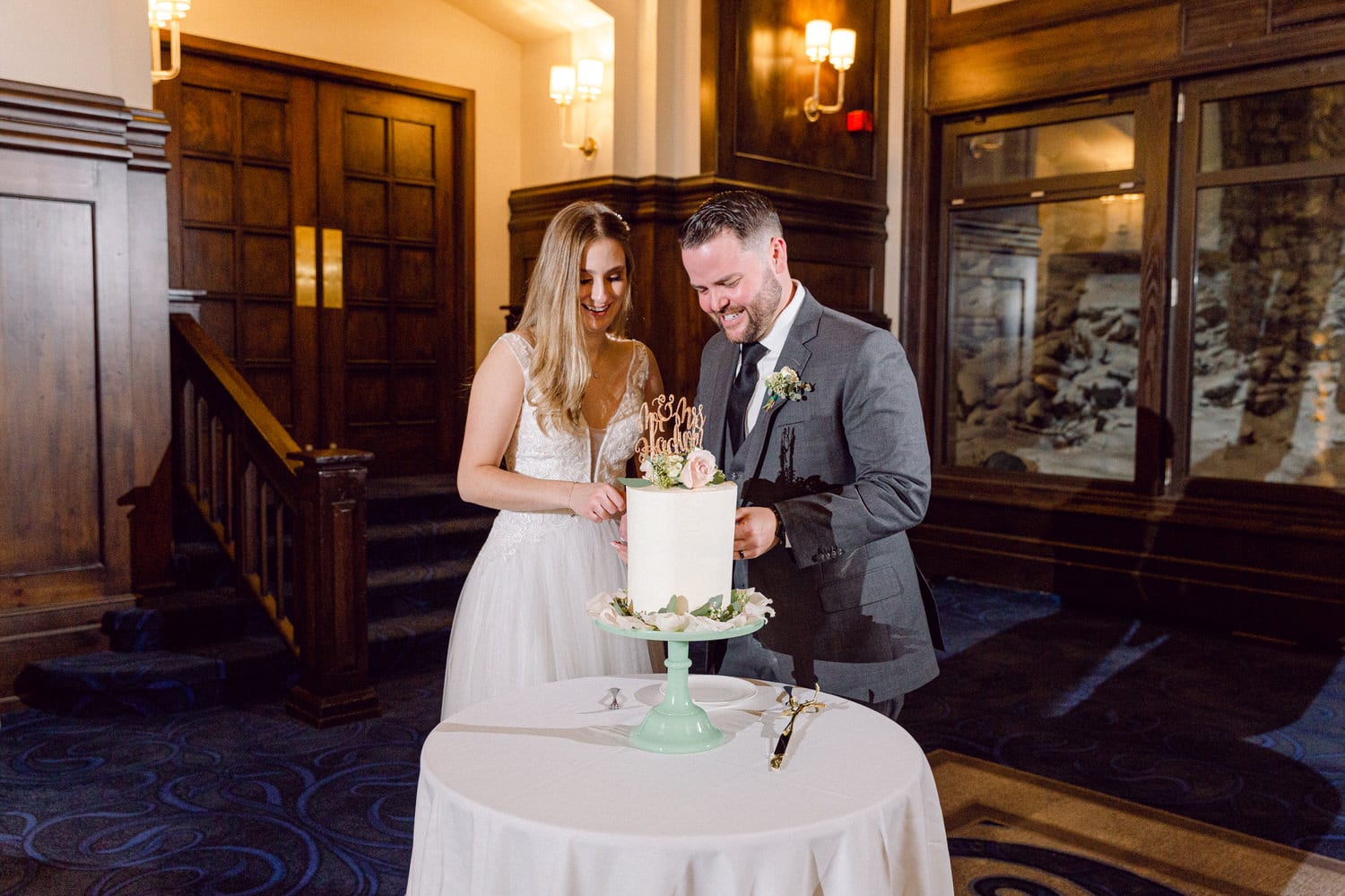 A happy couple sharing a moment while cutting their wedding cake at a beautifully decorated table in an elegant venue.