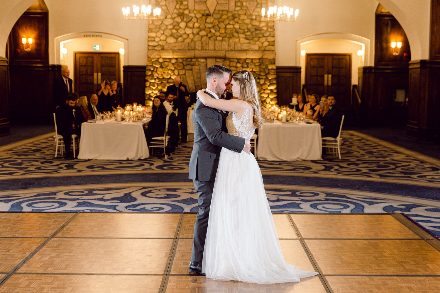 A bride and groom share a tender moment during their first dance, surrounded by elegantly set tables and guests enjoying the celebration.