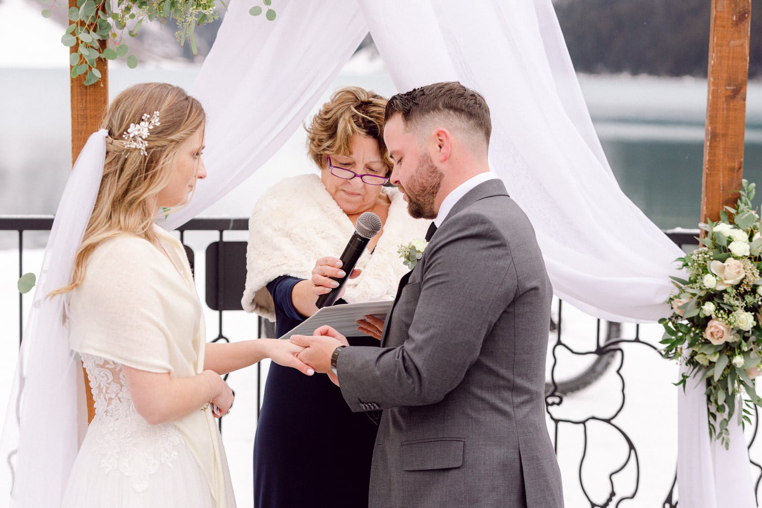 A bride and groom exchange vows during a winter wedding ceremony, with a celebrant officiating under a beautifully adorned arch.