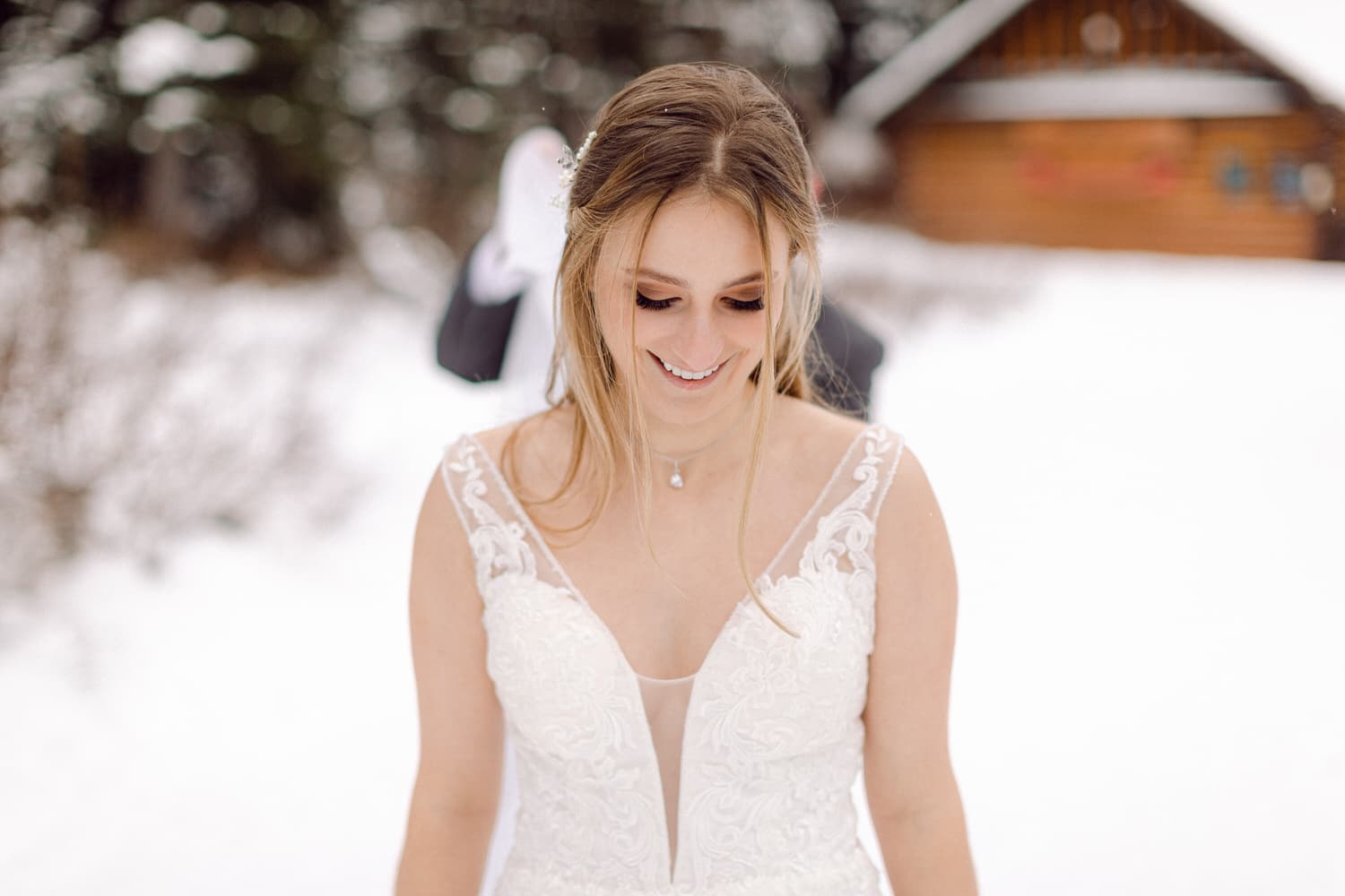 A happy bride in a white gown smiles serenely while standing in a snowy landscape, with a rustic cabin in the background.