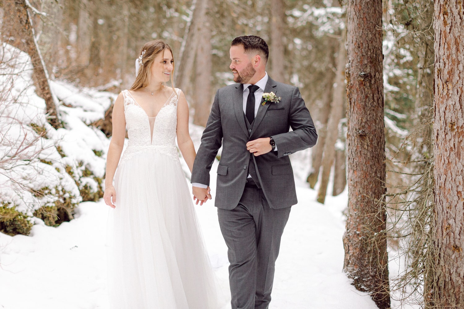 A couple walks hand-in-hand through a snowy forest, embracing their love on their wedding day.