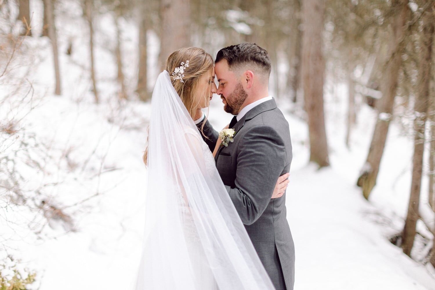 A couple embracing in a snowy forest, sharing an intimate moment on their wedding day.