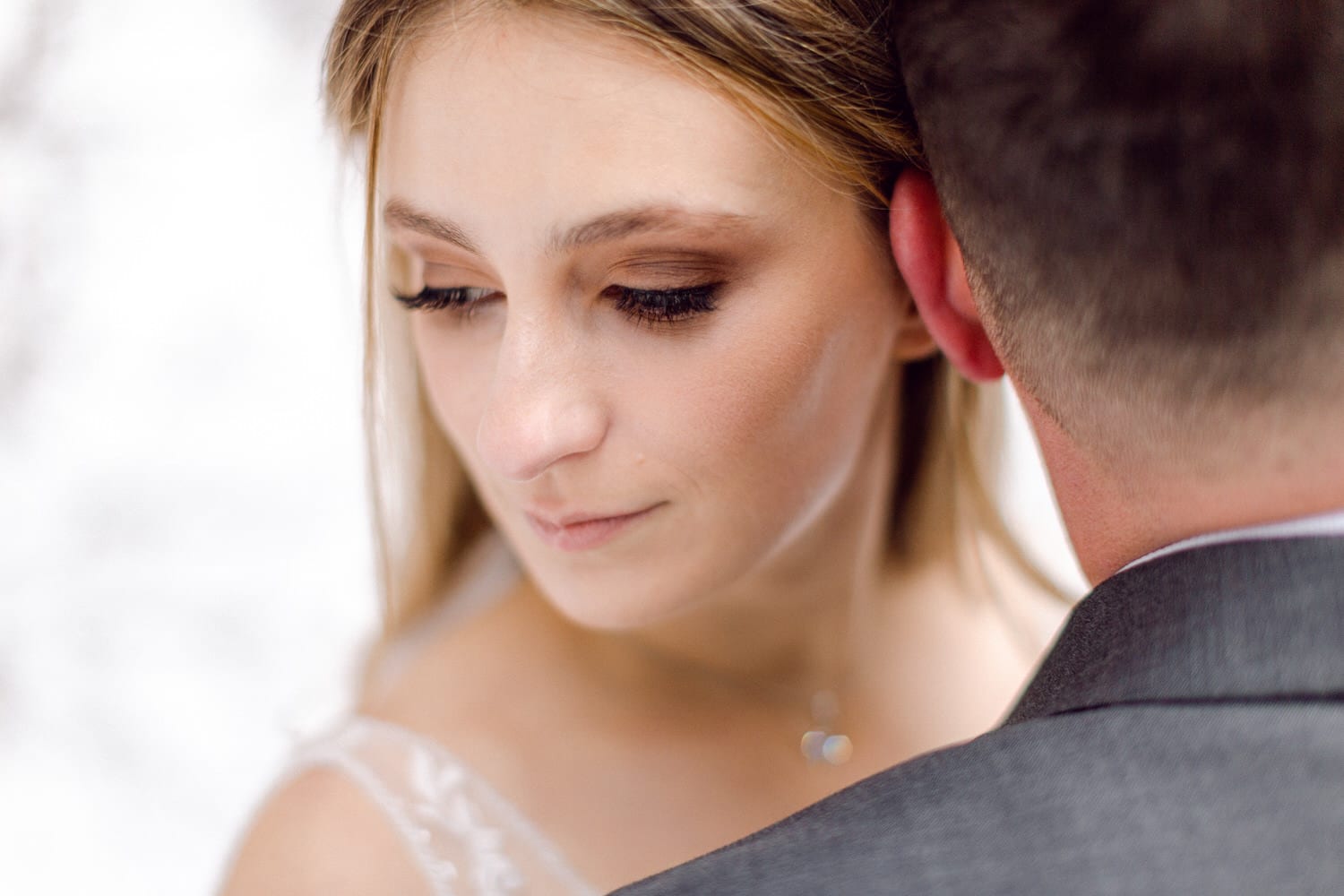 A close-up of a bride's profile as she shares a tender moment with her partner, showcasing soft makeup and delicate features against a blurred background.