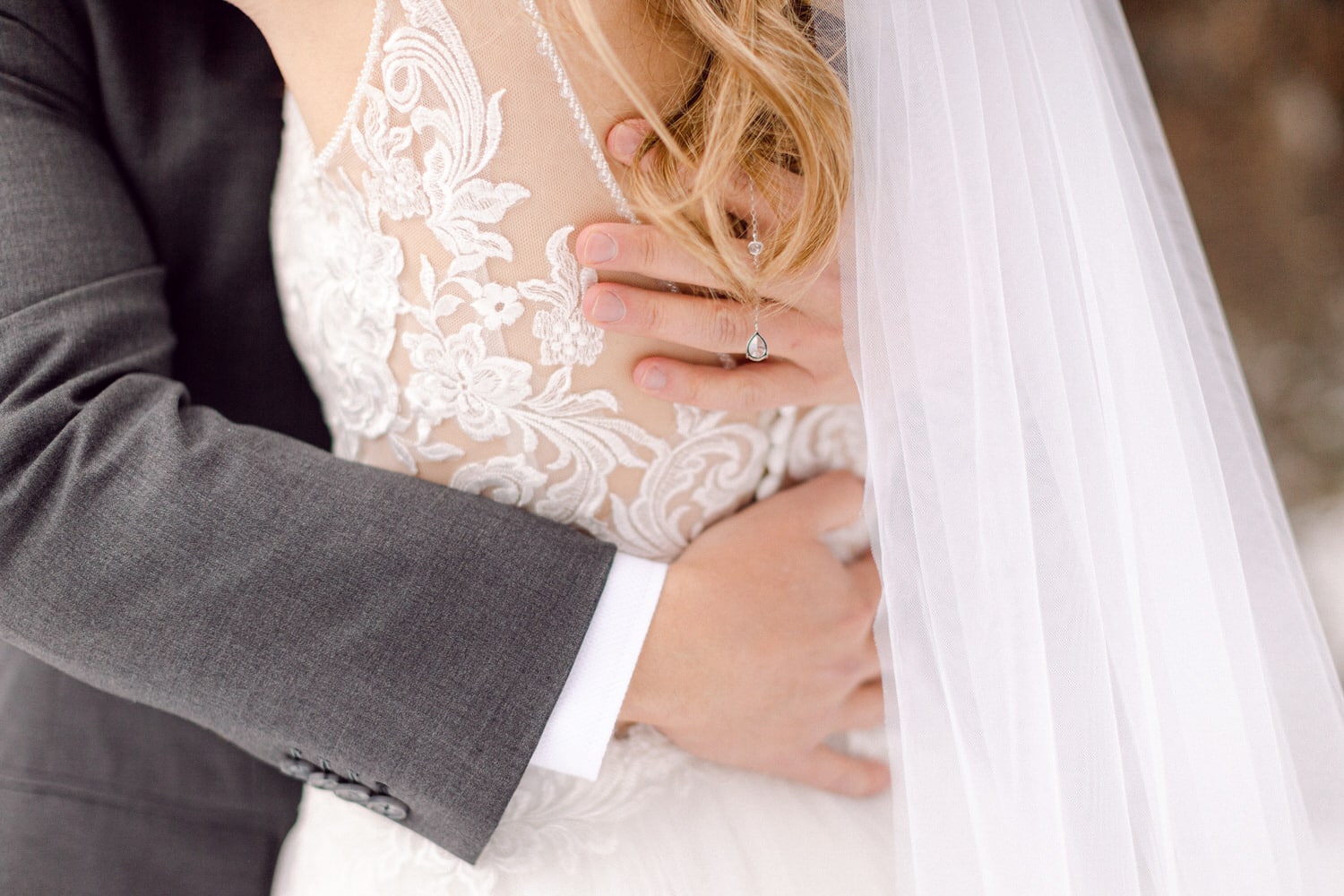 Close-up of a couple's embrace during a wedding, showcasing intricate lace details on the bride's dress and a wedding ring.