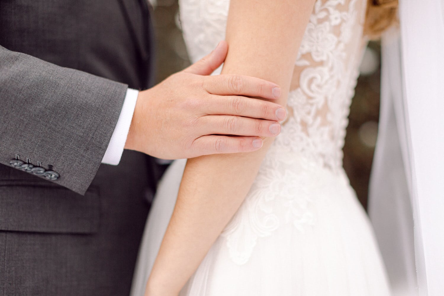 Close-up of a groom's hand gently resting on the bride's arm, showcasing elegance in their wedding attire.