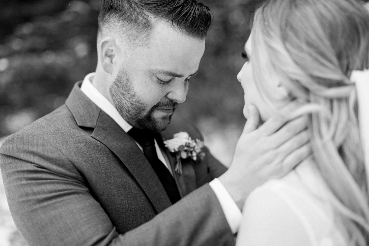 A man and woman share a tender embrace, with the man gently holding the woman's face, capturing a moment of love and closeness in a soft black and white photograph.