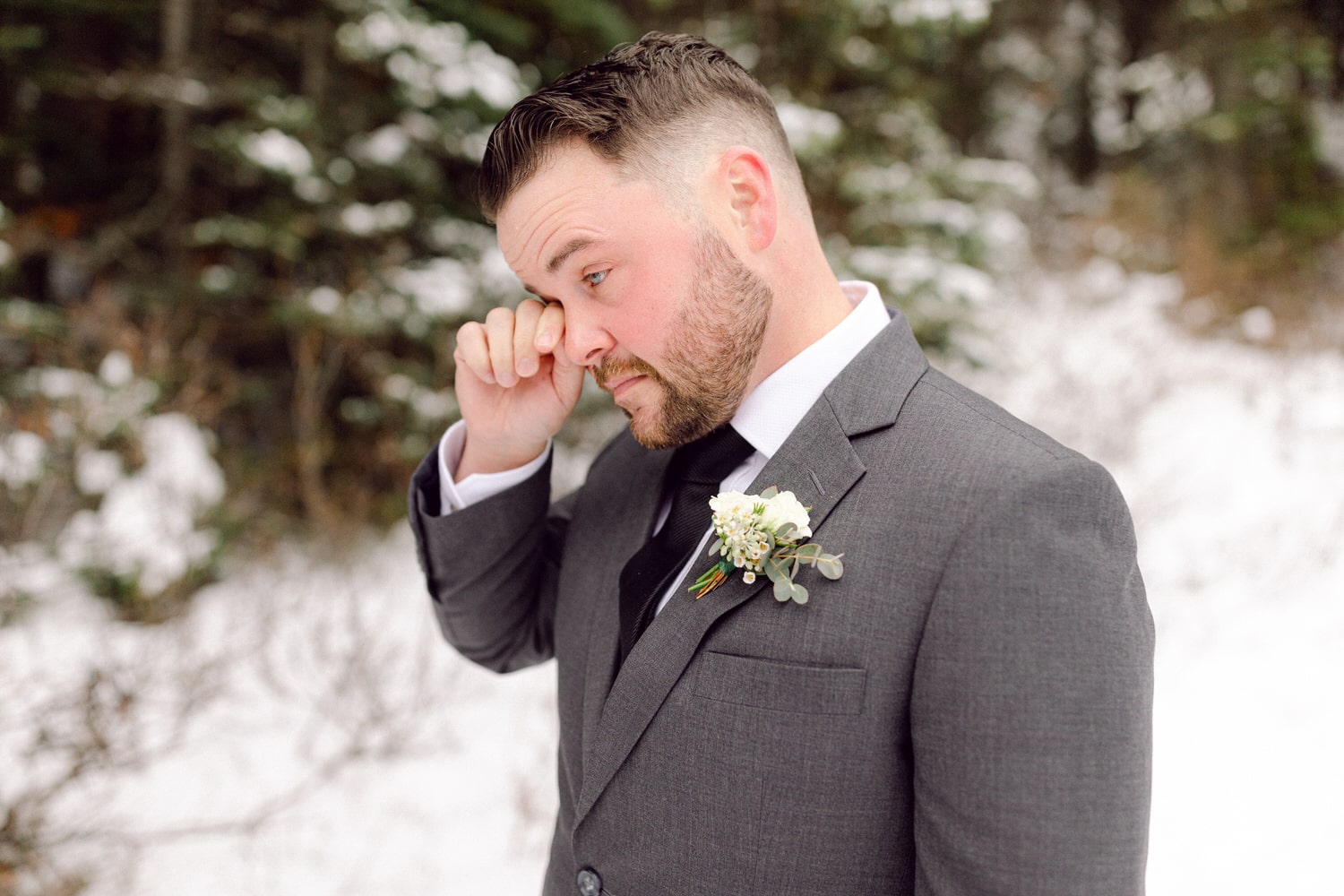 A man in a gray suit wipes away a tear in a snowy outdoor setting, highlighting a poignant moment.