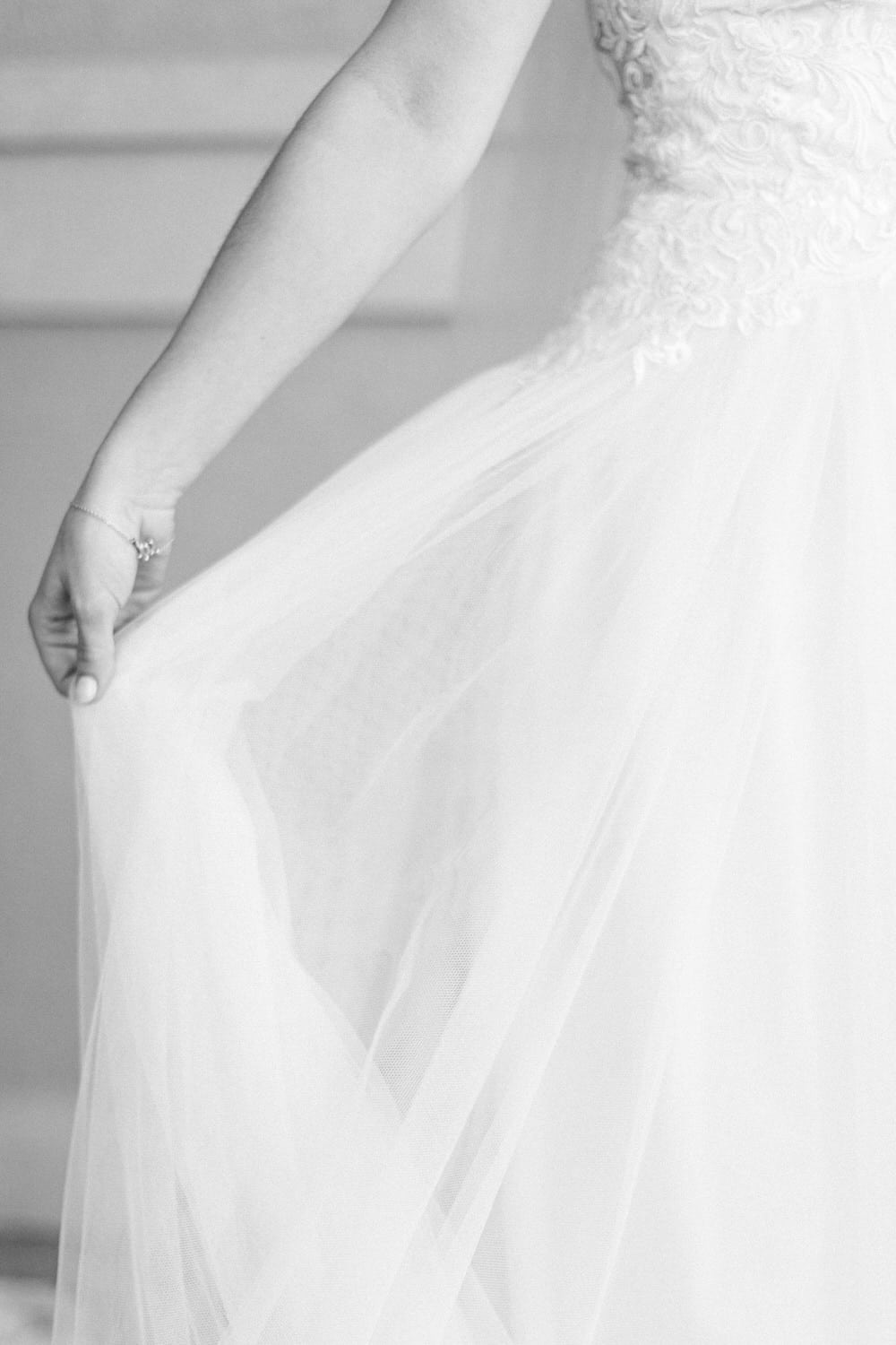 Close-up of a hand holding the flowing fabric of a wedding dress, showcasing intricate textures and soft layers.