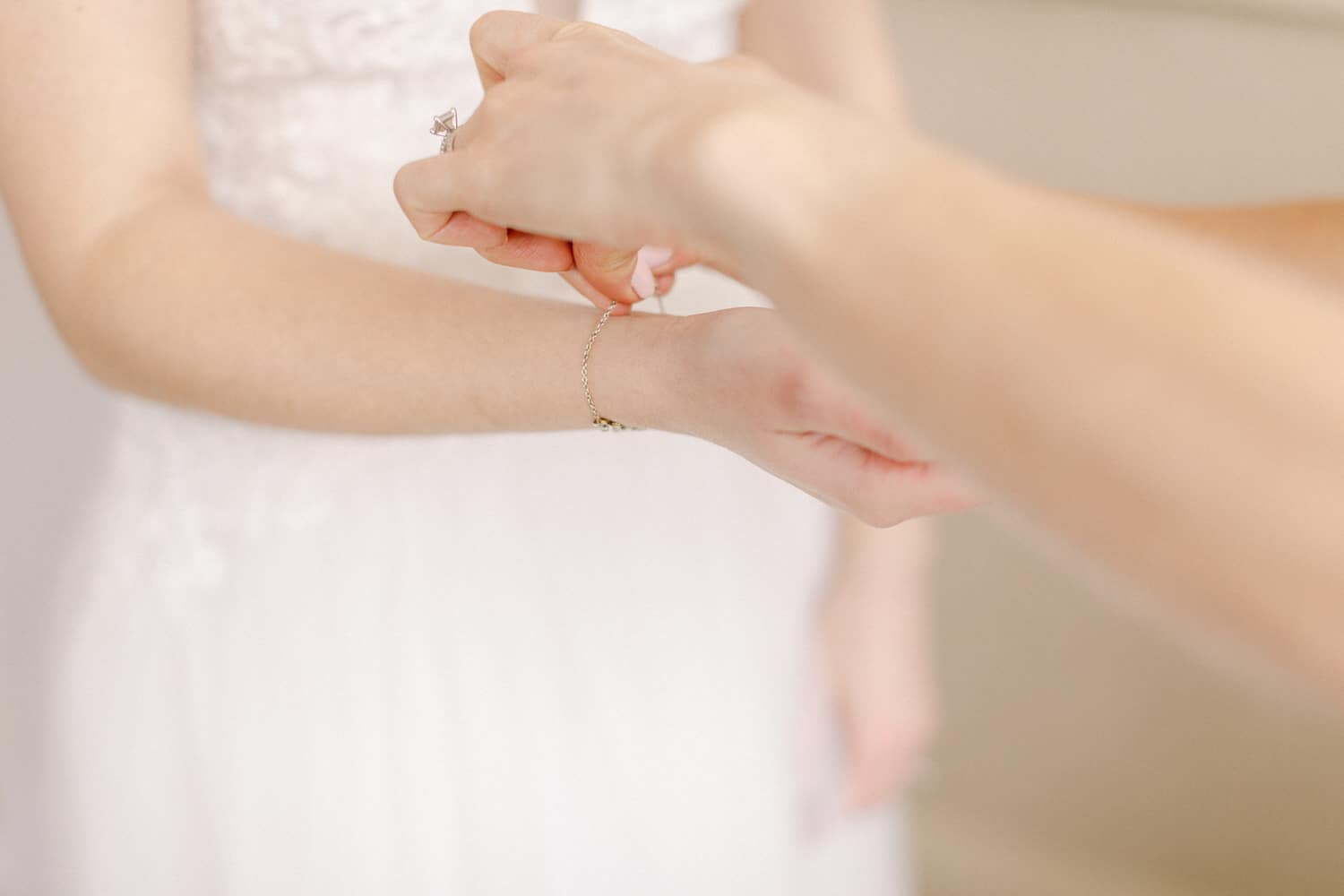 A close-up of a hand fastening a delicate bracelet on a bride's wrist, showcasing the intimacy of wedding preparations.