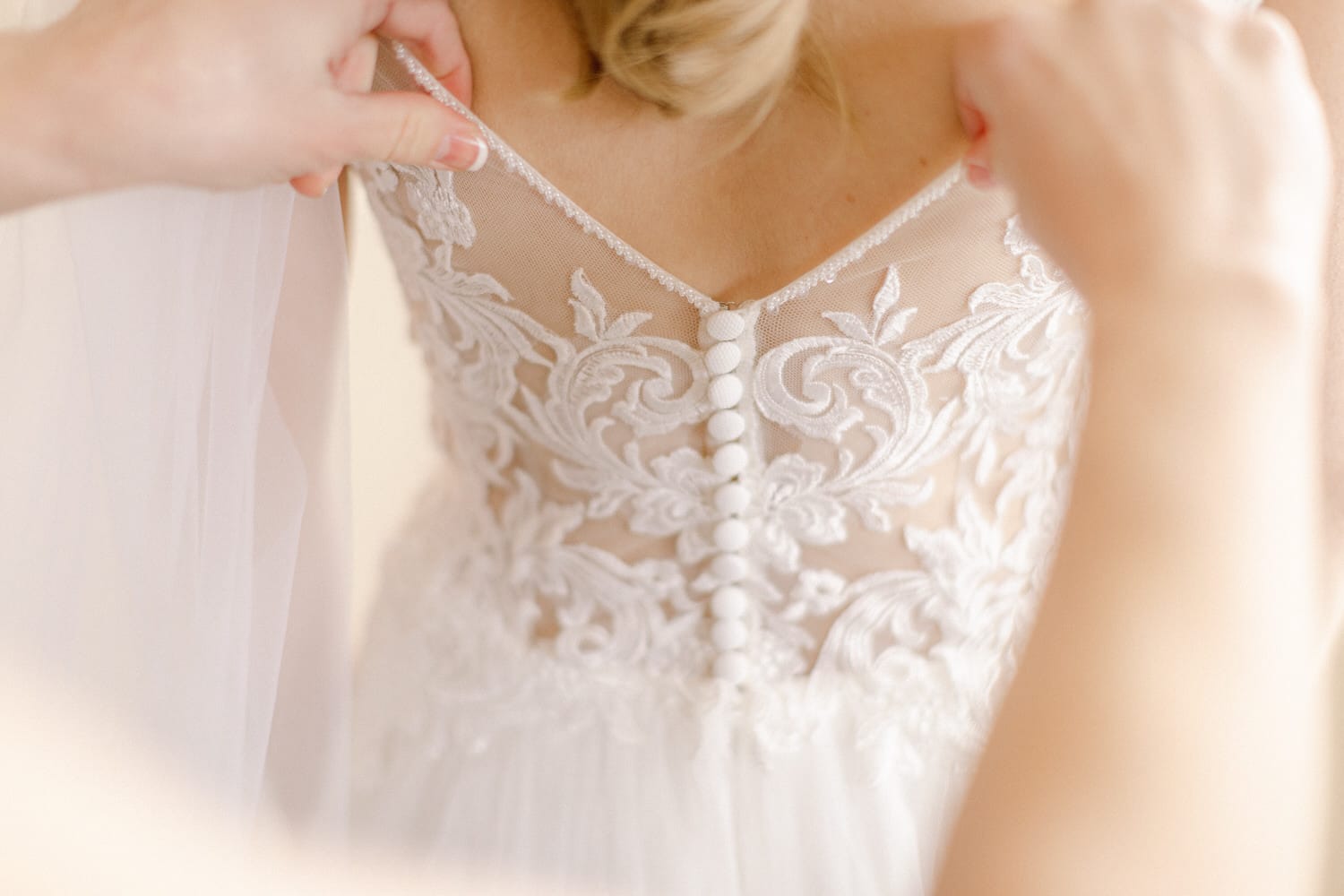 Close-up of a bridal gown's intricate lace back with buttons being adjusted by a hand.