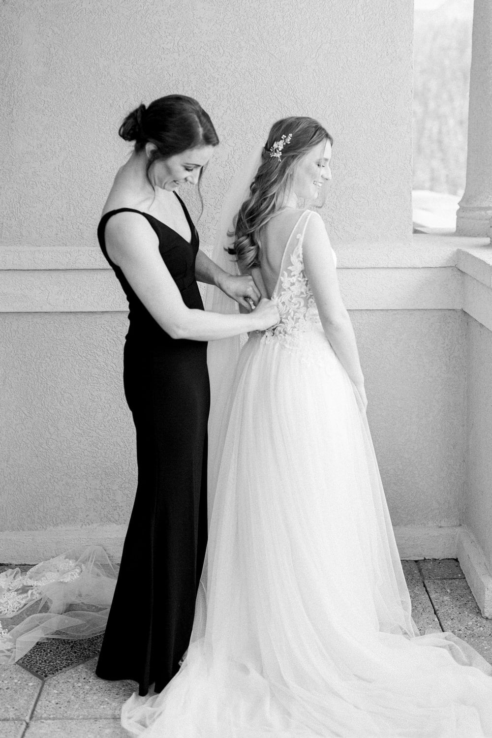 A bride being helped with her dress by a bridesmaid, capturing a moment of intimacy and support before the wedding ceremony.