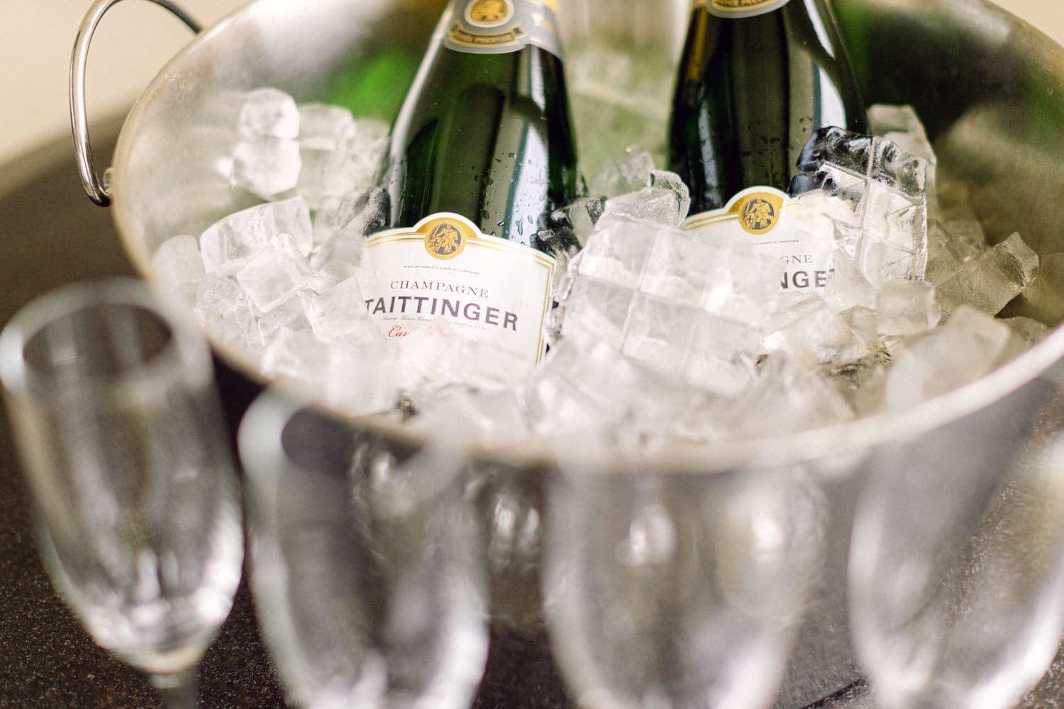 Two bottles of Taittinger champagne in a bucket filled with ice, surrounded by elegant champagne flutes.