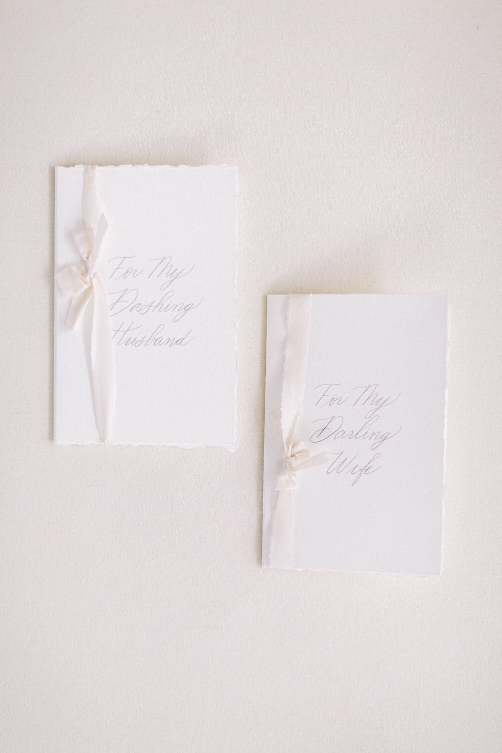 Two elegant greeting cards with pale ribbons, labeled "For My Dashing Husband" and "For My Darling Wife," set against a soft cream background.