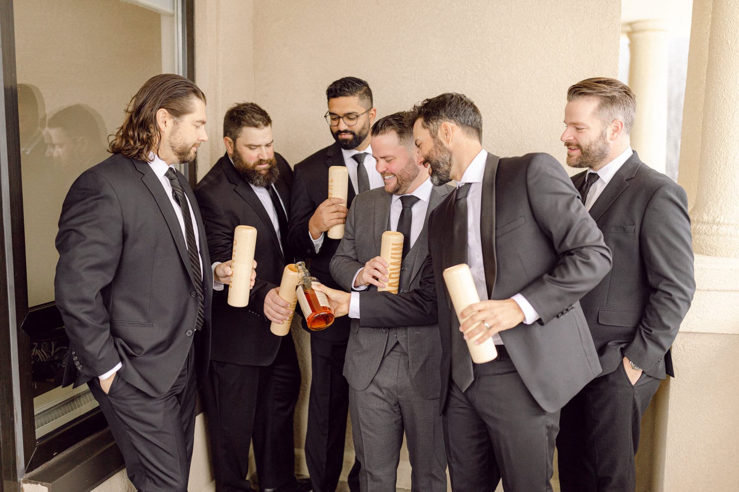 A group of well-dressed men in suits joyfully sharing drinks and wooden flasks during a wedding celebration.