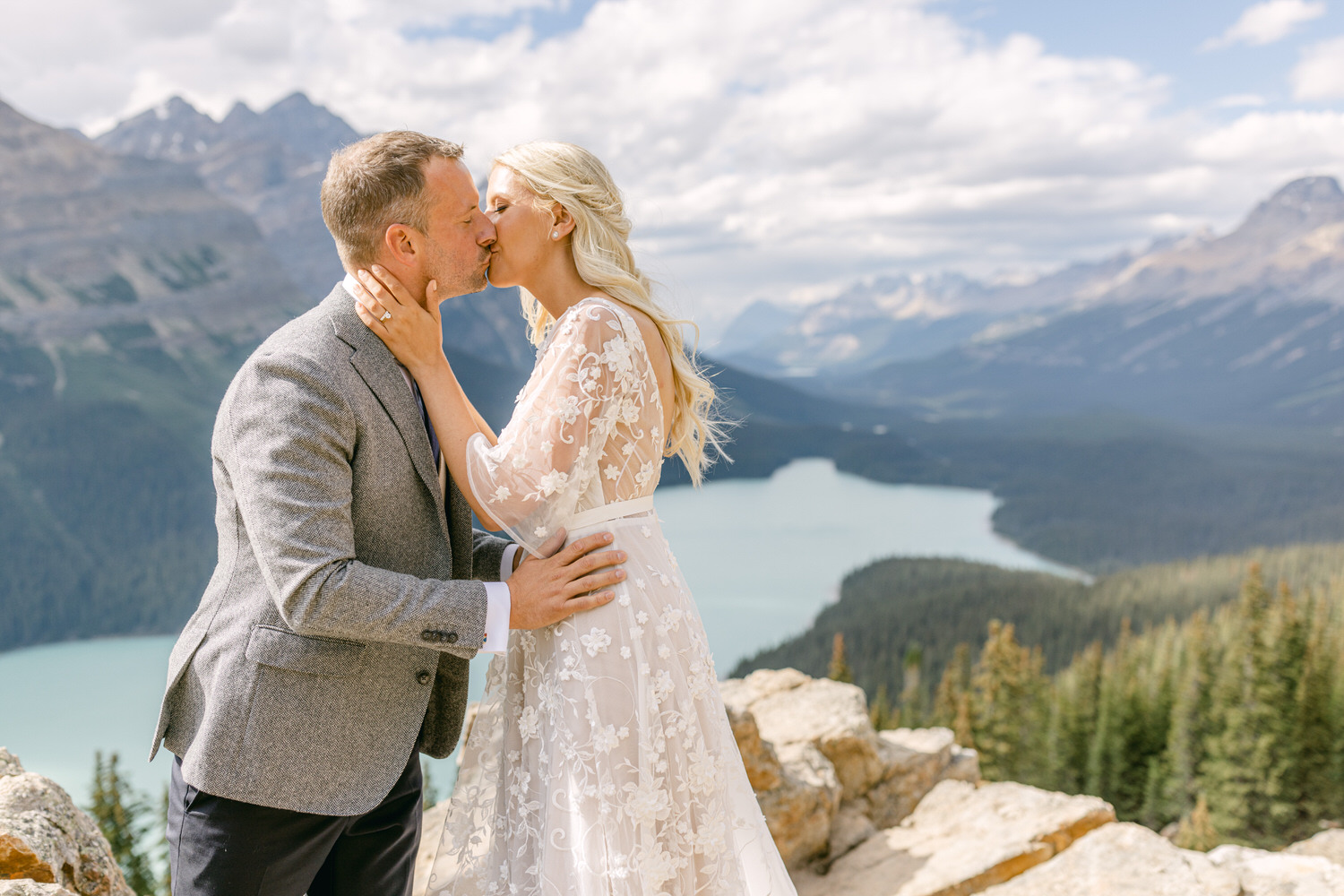 A couple sharing a romantic kiss with a stunning mountain landscape and lake in the background.