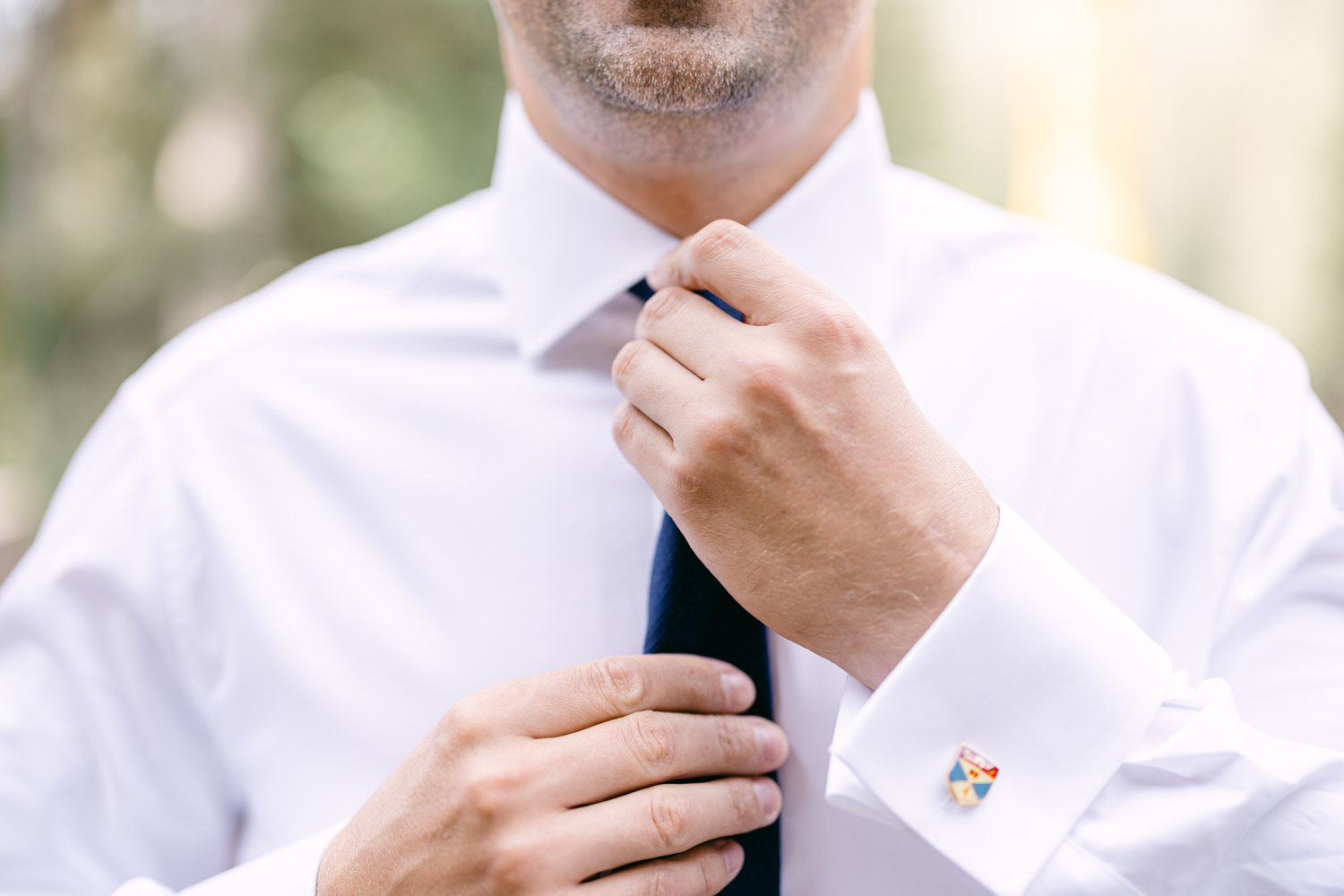 Close-up of a man adjusting his tie while wearing a crisp white shirt with a decorative cufflink.