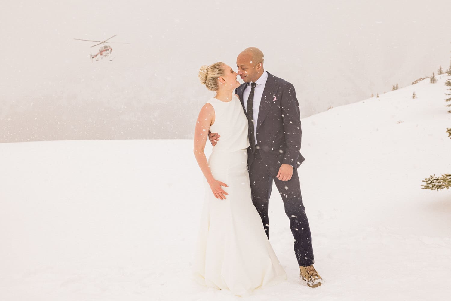 A couple sharing a romantic moment in a snowy landscape, with a helicopter flying in the background.