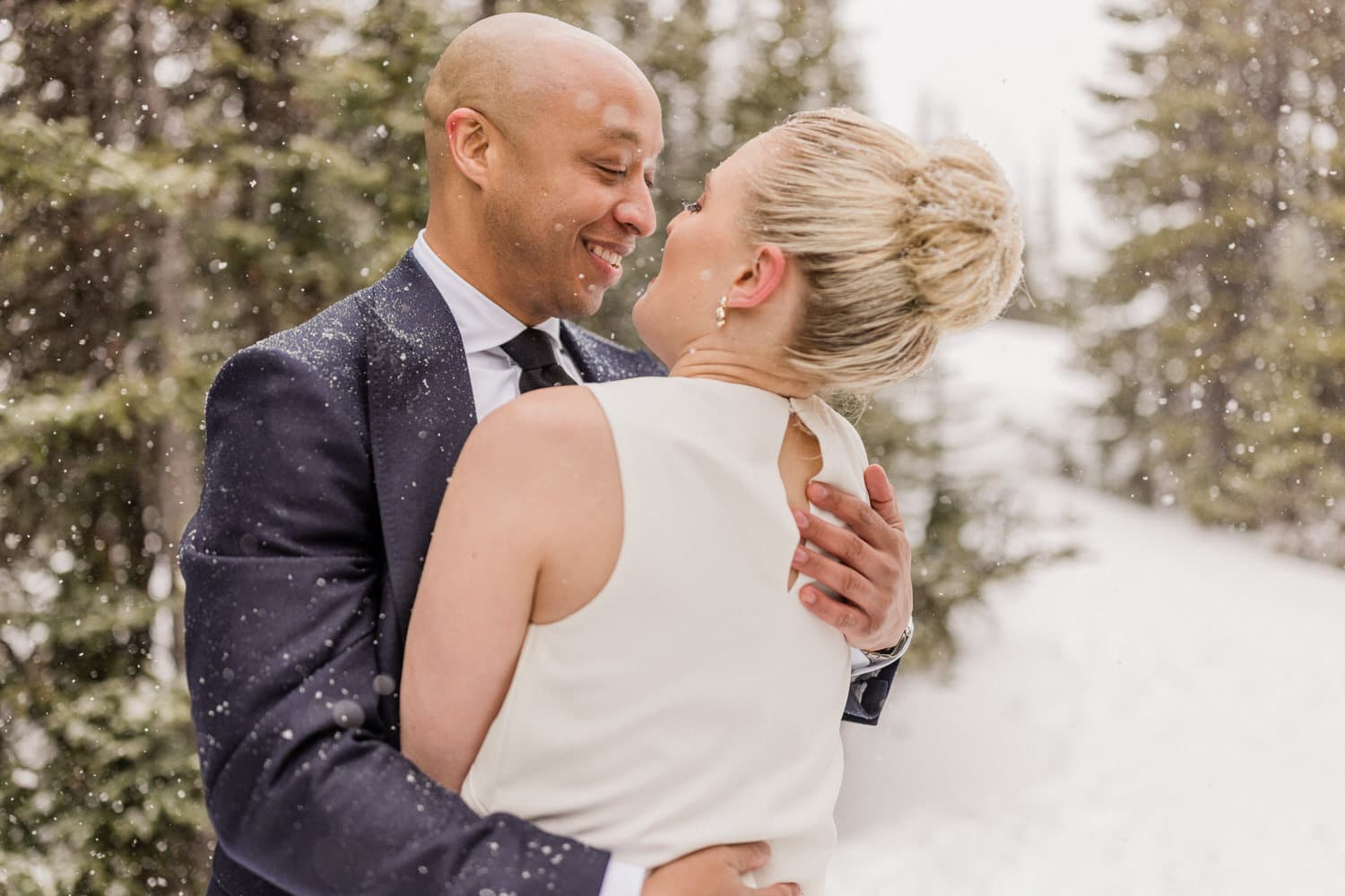 A joyful couple embracing in a snowy forest setting, capturing a moment of love amidst falling snowflakes.