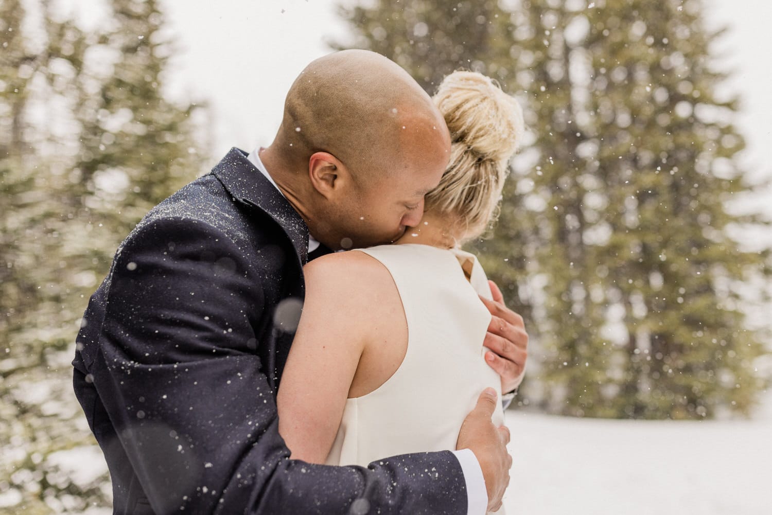 A couple shares a tender moment outdoors in a snowy landscape, capturing their love and affection against a backdrop of pine trees.