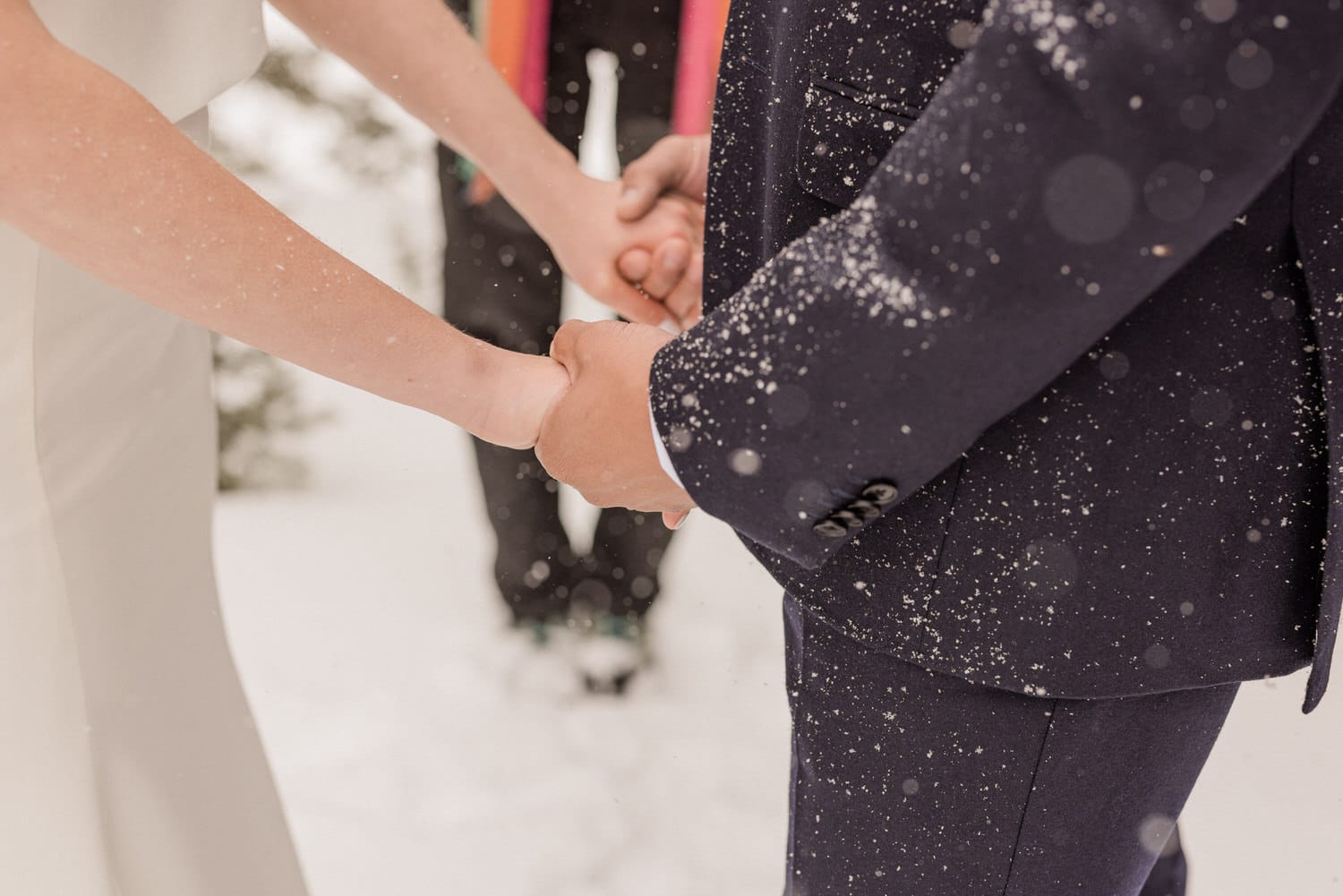 A bride and groom holding hands in the snow during their wedding ceremony, surrounded by gentle snowfall.