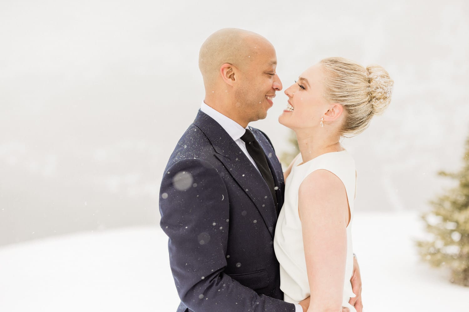 A joyful couple sharing an intimate moment in a snowy setting, smiling at each other while surrounded by a winter wonderland.