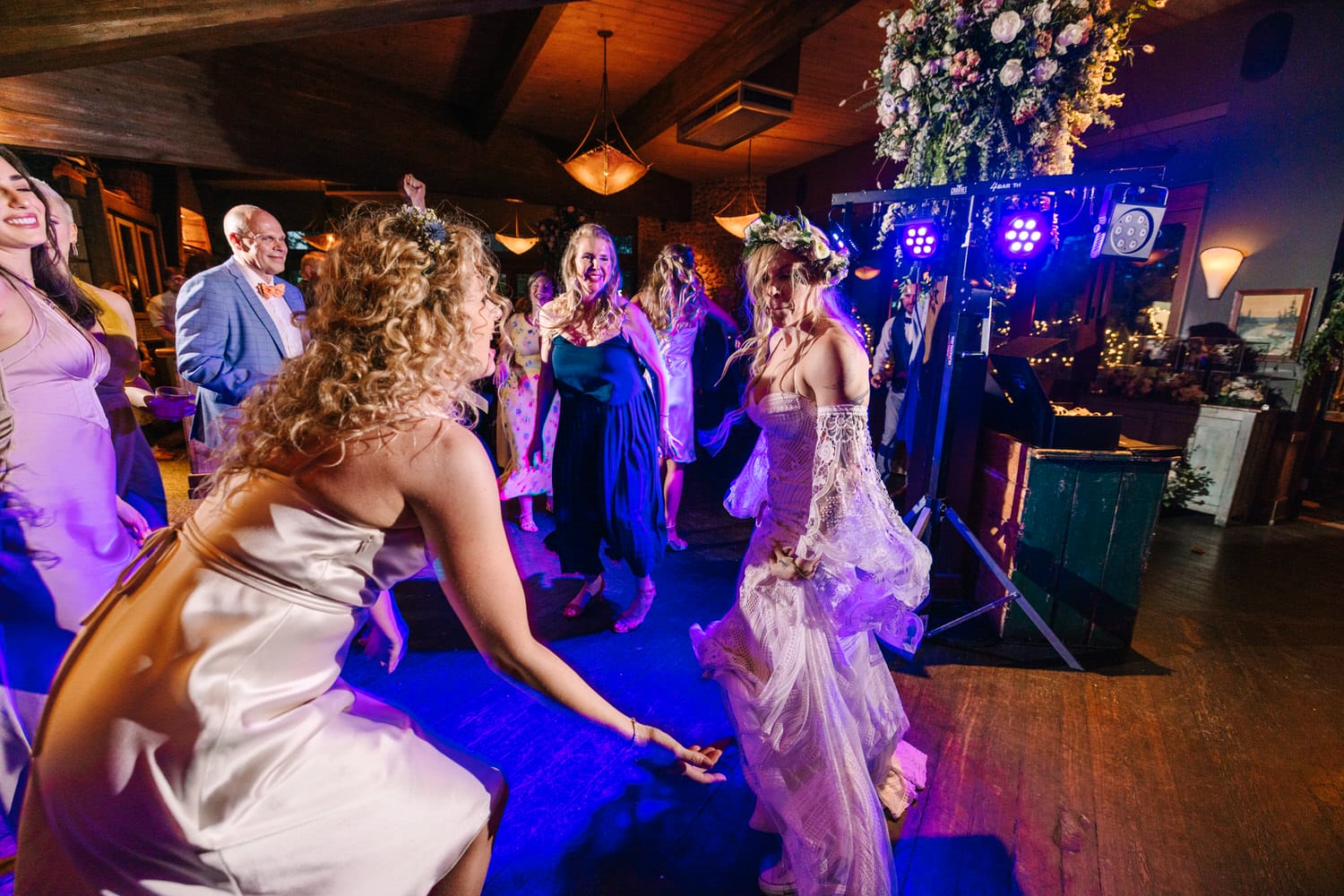 A joyful group of guests dancing at a wedding reception, with vibrant lights and floral decorations in a lively atmosphere.