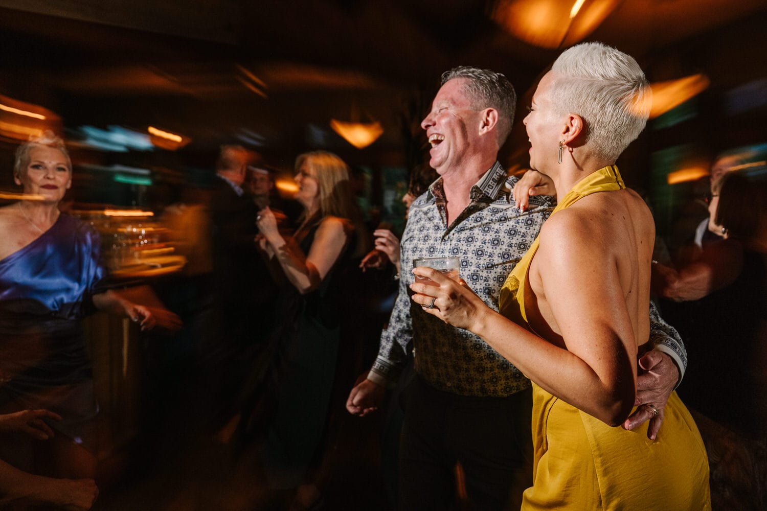 A lively scene of people dancing and enjoying themselves at a celebration, with a focus on a joyful couple in the foreground.