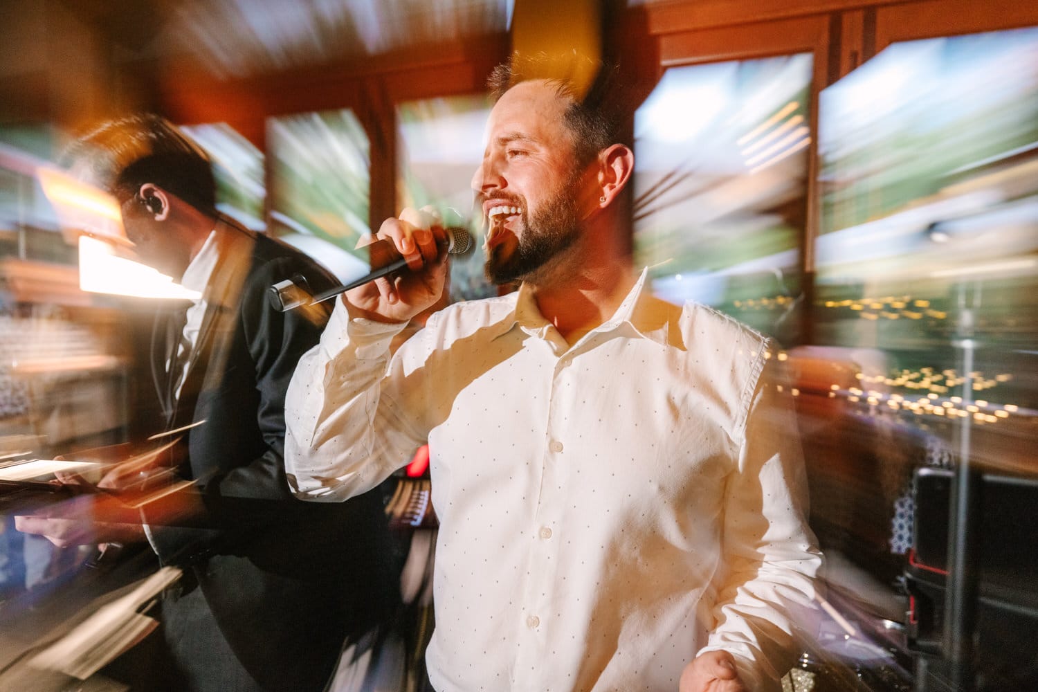 A man passionately singing into a microphone with a blurred background, depicting dynamic movement and excitement during a live event.